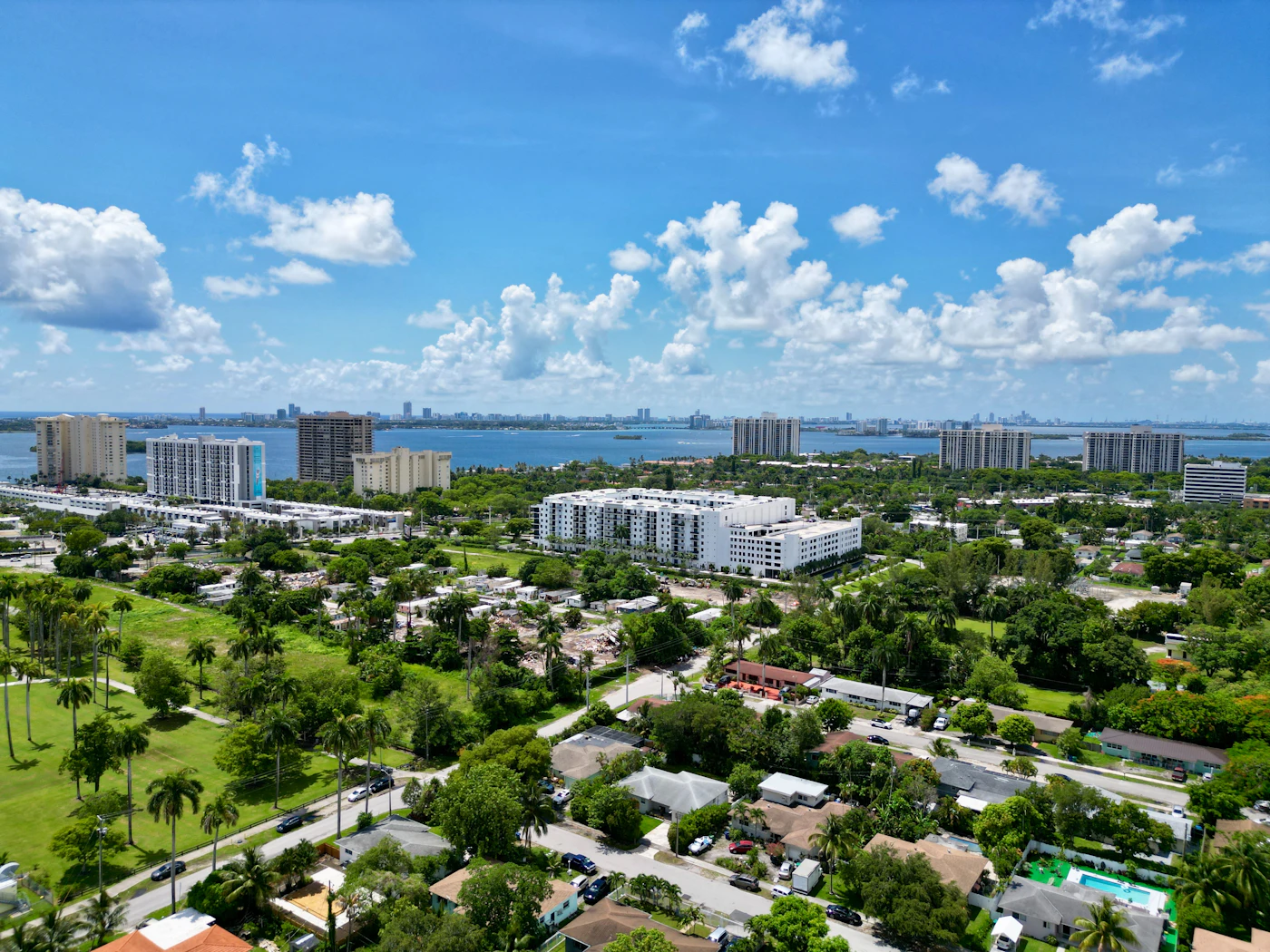 Aerial view of single-family homes and tile roofs in a Miami neighborhood, with Biscayne Bay and the skyline behind